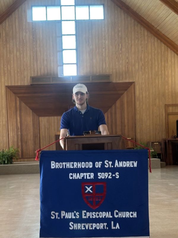 Man standing behind a Brotherhood of St. Andrew banner in a church.
