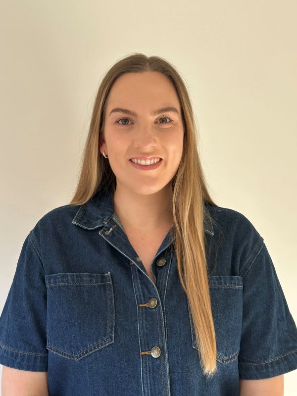 Smiling woman in denim jacket against plain background.