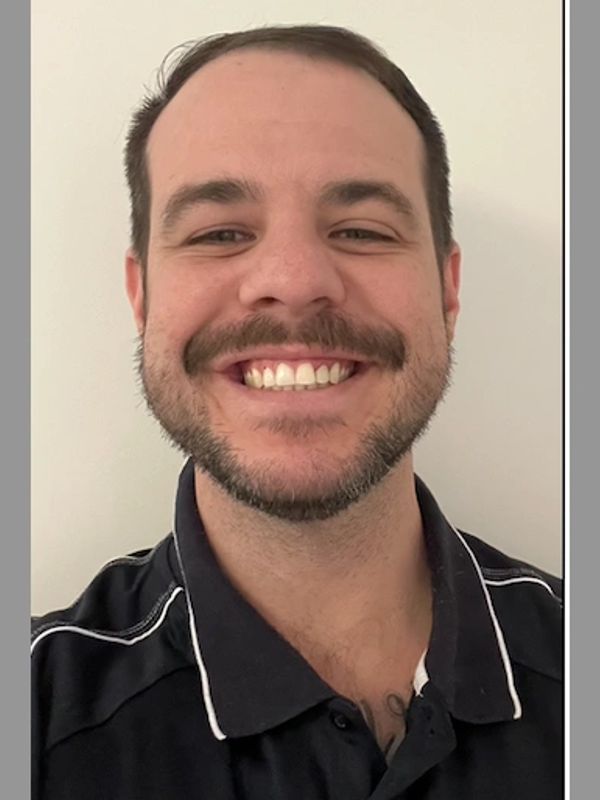 Smiling man with beard and black collared shirt.