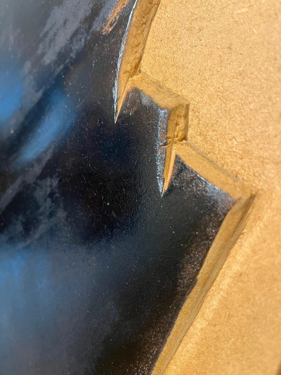 Close-up of a black painted surface with sharp, jagged edges on a tan background.