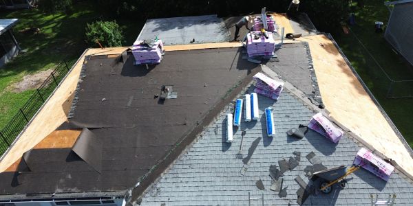 A house roof partially covered with black roofing felt and stacks of roofing materials.