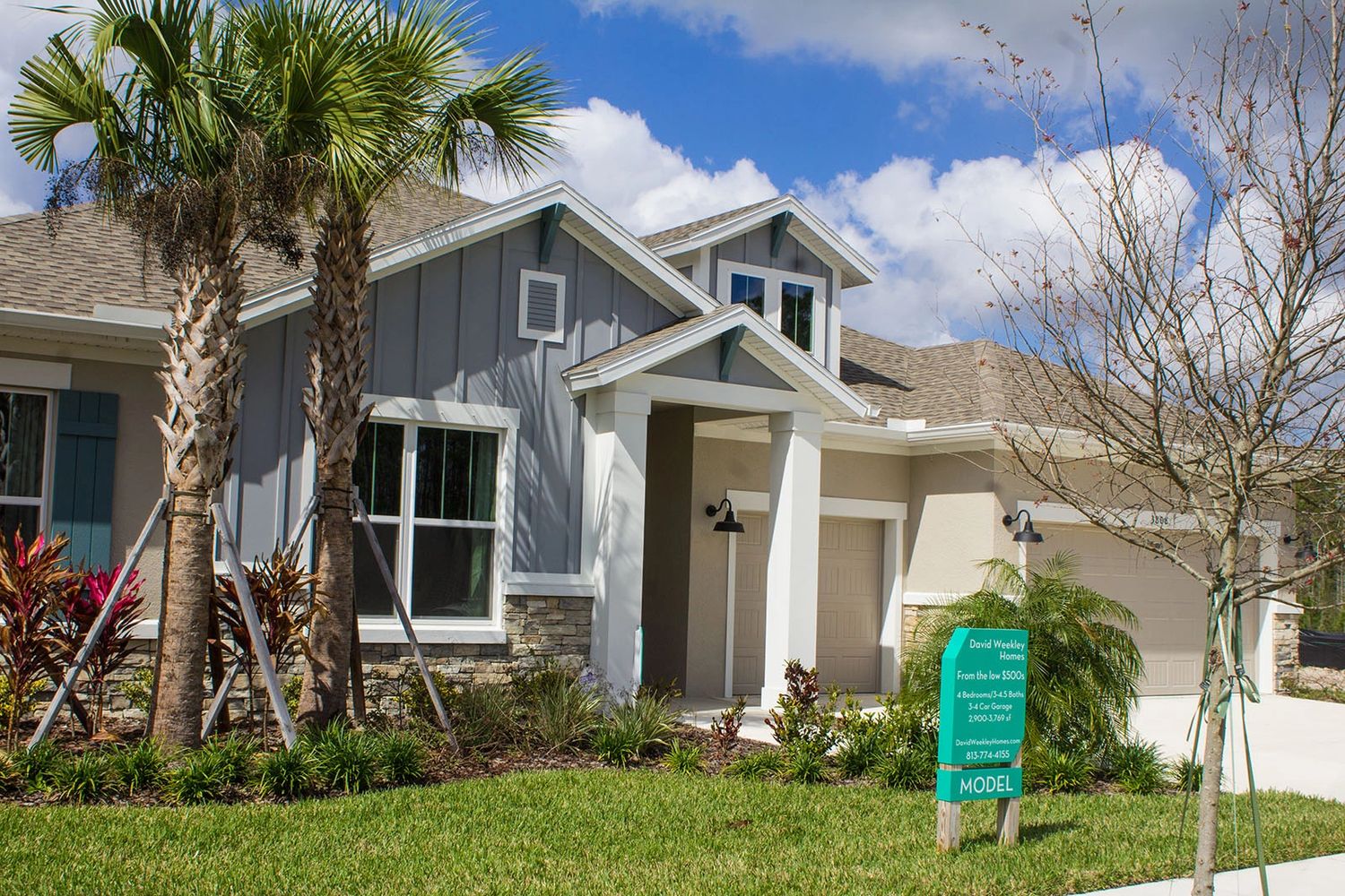 Modern model home with palm trees and a manicured lawn under a bright blue sky.