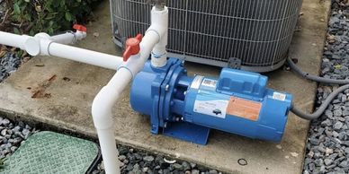 Blue water pump connected to white PVC pipes on a concrete slab.