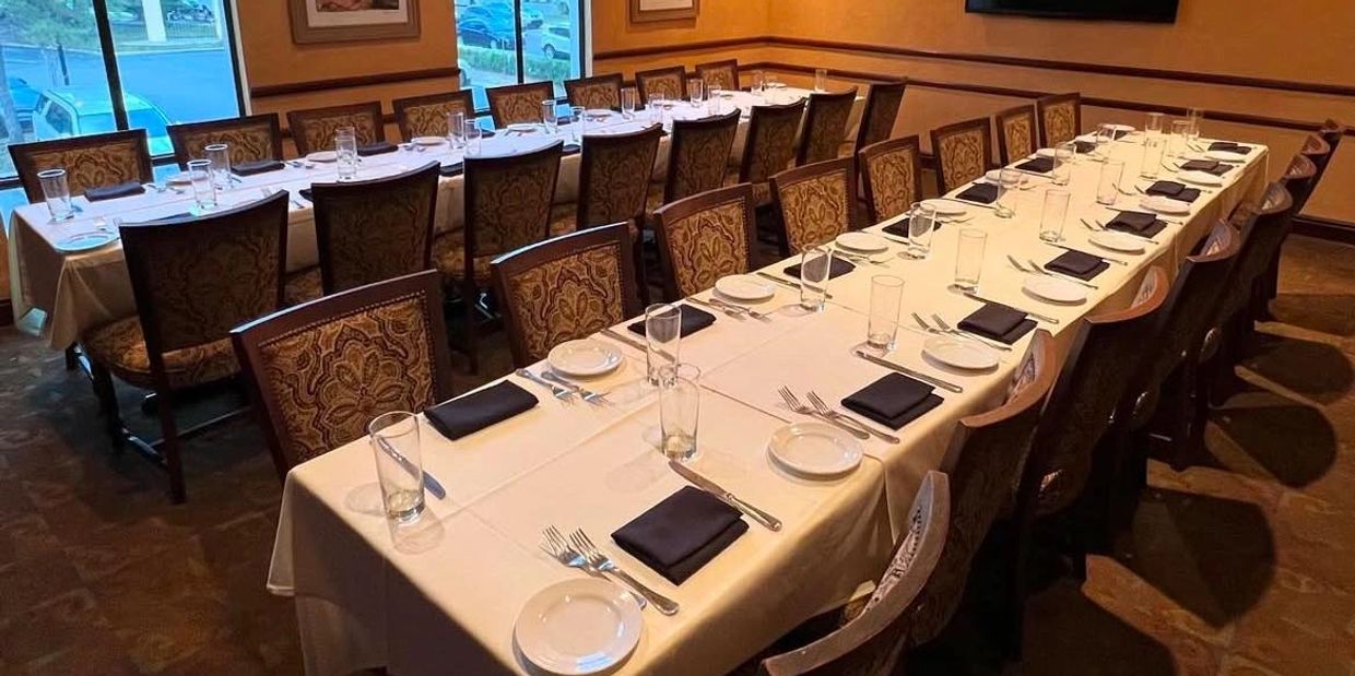 Two long dining tables set with plates, glasses, and black napkins in an elegant room.