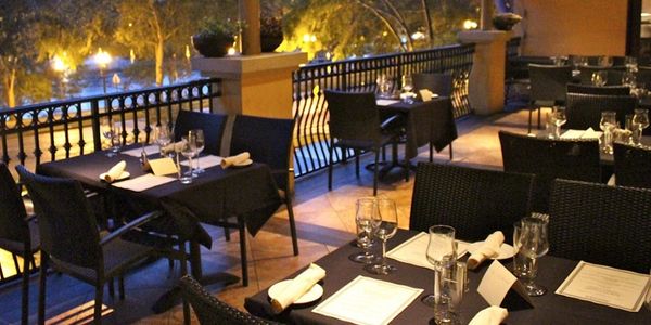 Evening outdoor dining area with tables set with black tablecloths and glassware.