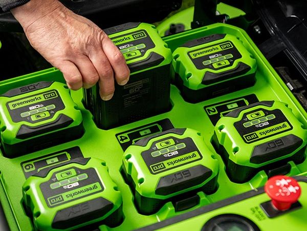 Hand placing a Greenworks Pro 60V battery into a charging station.