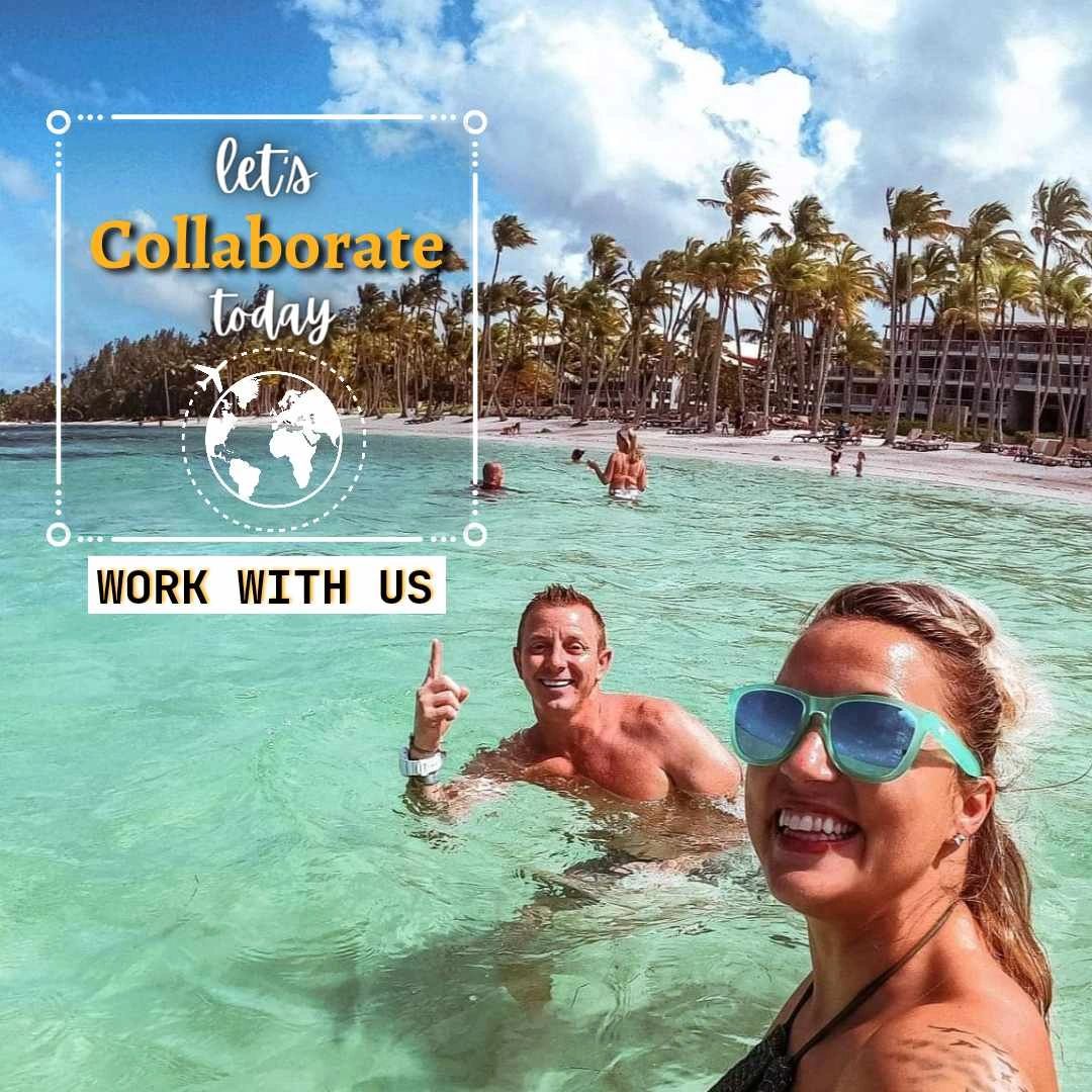 man and woman swimming in the ocean, smiling and pointing to a 'work with us' sign
