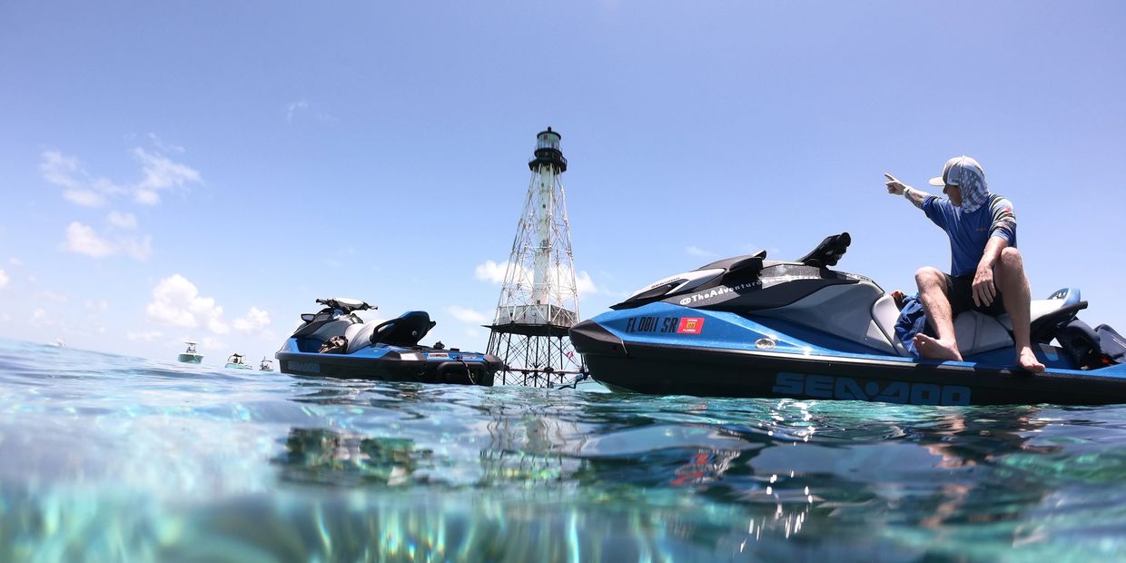 man sitting on a jet ski in the ocean pointing at a light house