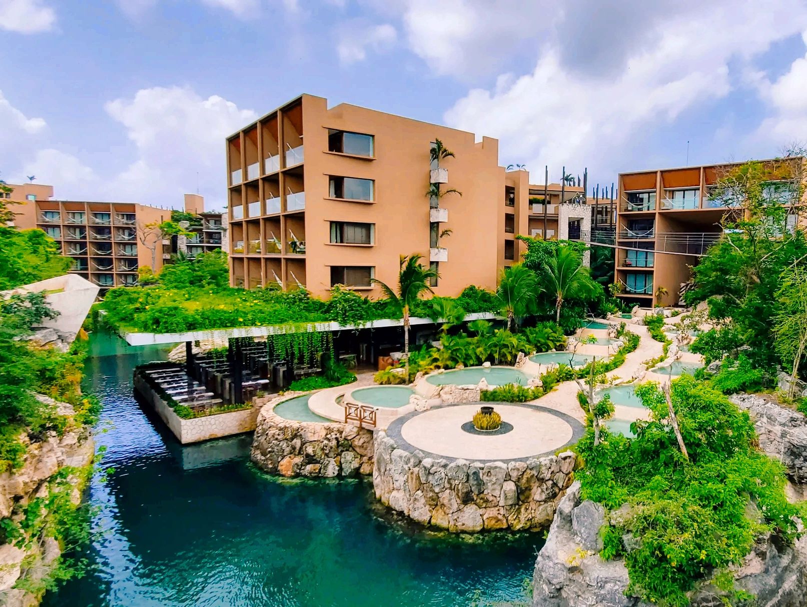A small section of Hotel Xcaret with a large orange building sitting next to multiple water features
