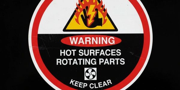 Warning sign for hot surfaces and rotating parts, advising to keep clear.