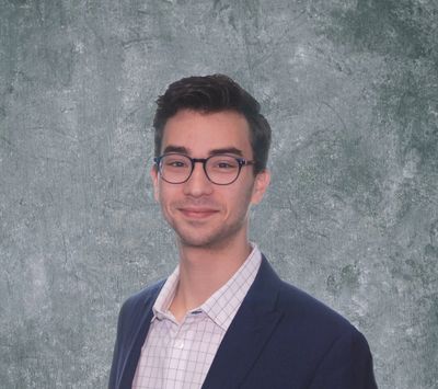 Young man with glasses in formal attire smiling.