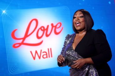Woman smiling in front of a 'Love Wall' sign.