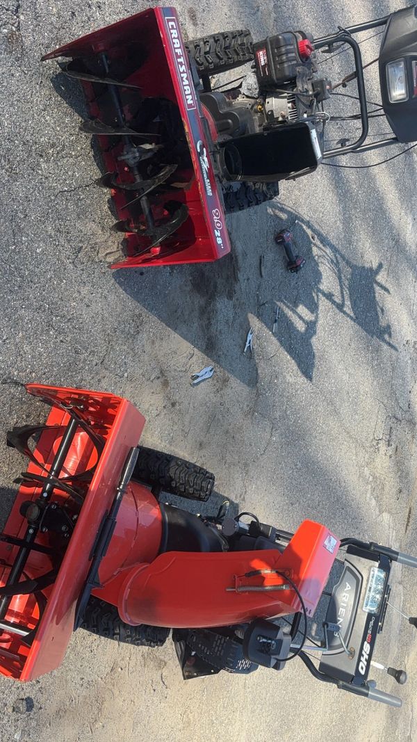 Two snow blowers, one Craftsman and one Ariens, on a customers driveway with tools around.