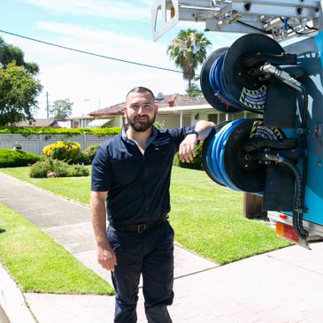 Man standing next to a truck with blue hose reels on a sunny day.