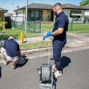 Two workers inspecting a street drain with specialized equipment.