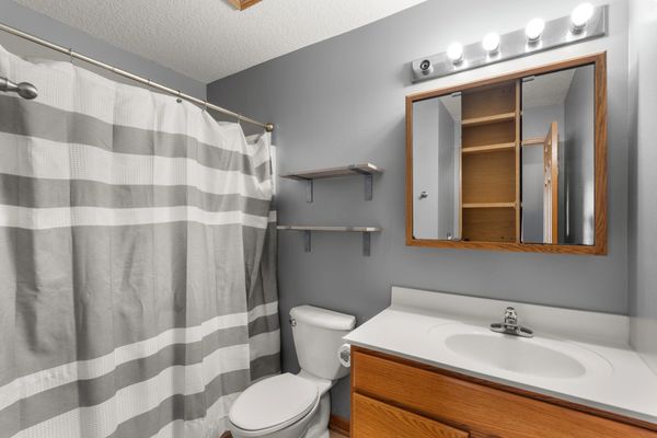 Clean bathroom with gray and white striped shower curtain, wooden vanity, and wall shelves.