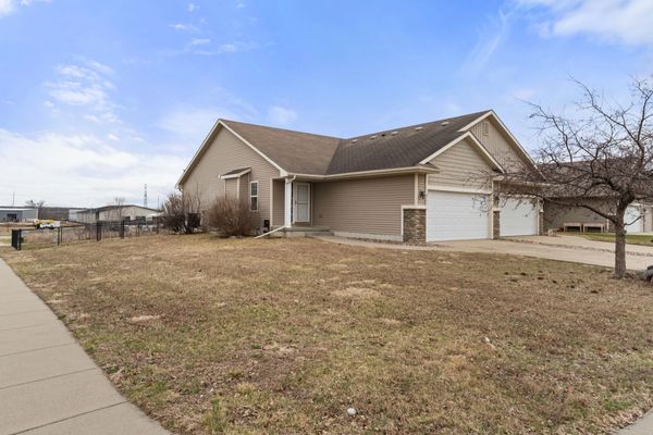A beige suburban house with a large garage and dry lawn under a partly cloudy sky.