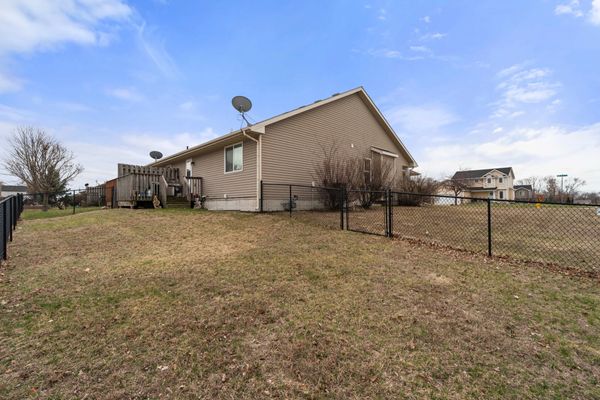 A single-story house with beige siding and a fenced yard under a blue sky.