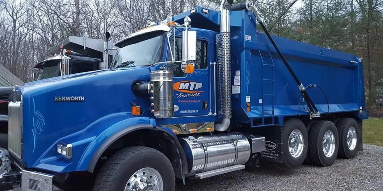 Blue Kenworth dump truck with four rear wheels parked outdoors.
