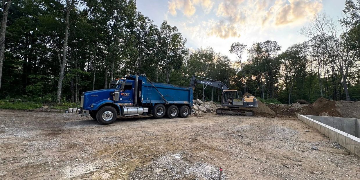Blue dump truck and excavator working at a construction site surrounded by trees.