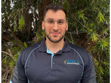 Man in a black STEP 1 Physiotherapy shirt outdoors.