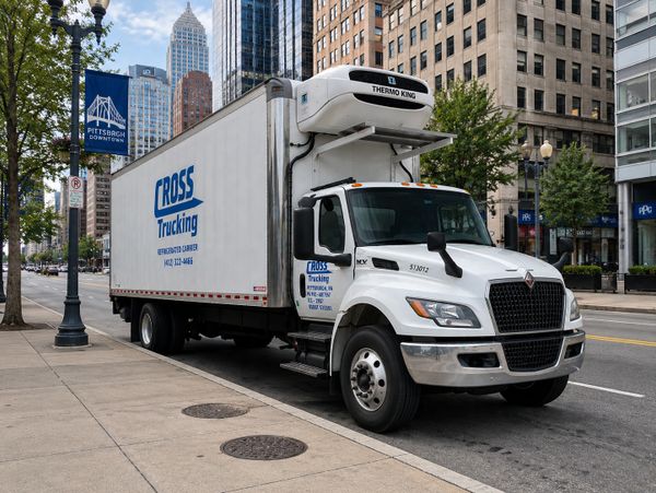 A white refrigerated Cross Trucking truck parked on a city street.