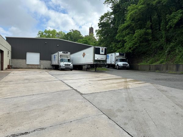 Refrigerator trucks parked outside a warehouse surrounded by trees