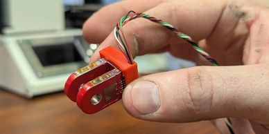 Hand holding a small red electronic sensor with wires.
Small Transducer, Micro size Strain Gauge ins