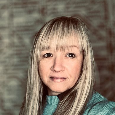 Portrait of a woman with long blonde hair and bangs wearing a teal sweater.