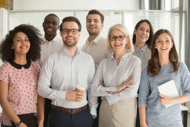 A diverse group of seven professionals smiling in an office setting.