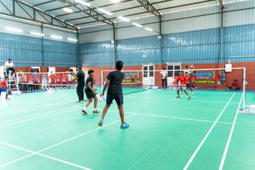 Indoor badminton game with players in action on a green court.