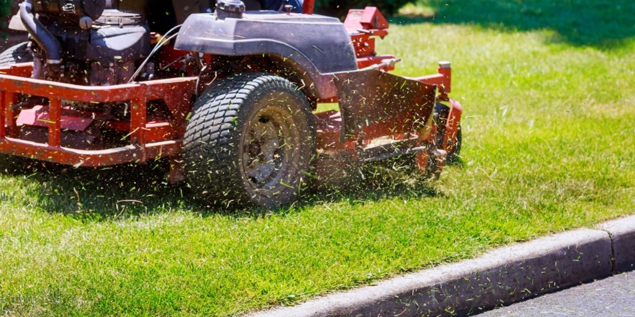 Close-up of a lawn mower cutting grass near a curb.