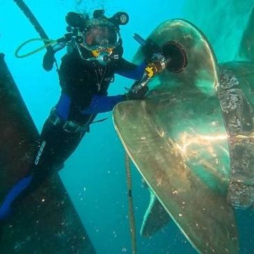 Diver cleaning a large ship propeller underwater.