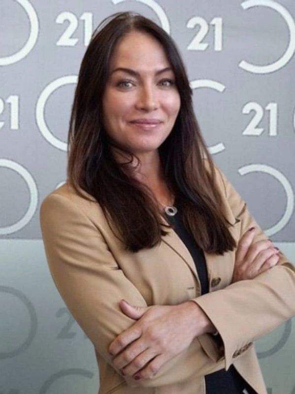 Confident woman in a tan blazer with arms crossed, smiling.