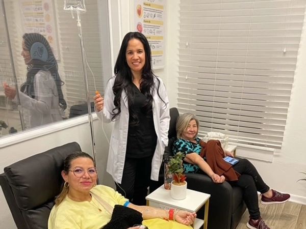 A smiling provider standing with two patients receiving IV therapy in reclining chairs 