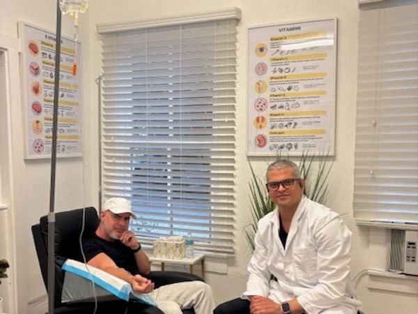 A patient receiving IV therapy seated next to a smiling provider