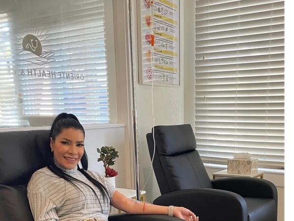 A smiling patient seated in a reclining treatment chair   receiving IV therapy at Oriente Health & W