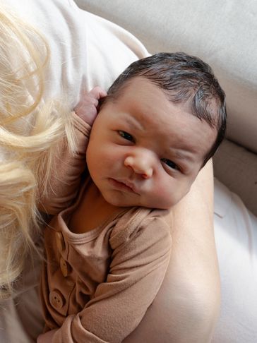 A newborn baby resting in someone's arms, looking curious.