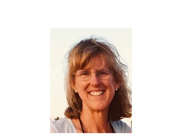 Smiling woman with glasses outdoors at sunset.