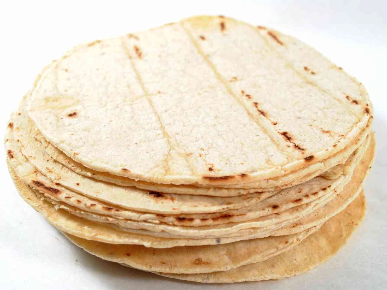 Stack of plain corn tortillas on a white surface.