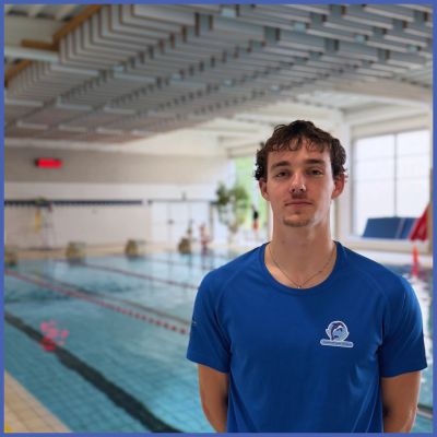 Young male lifeguard standing near an indoor swimming pool.