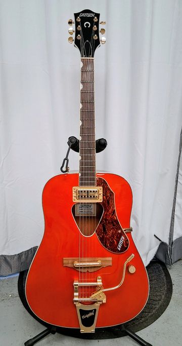 Bright orange Gretsch acoustic guitar with gold hardware and a Bigsby vibrato tailpiece.