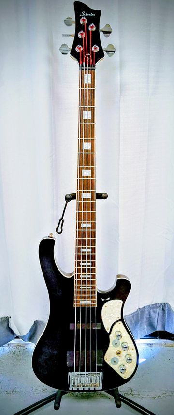 A black Schecter electric bass guitar with white inlays and control knobs.