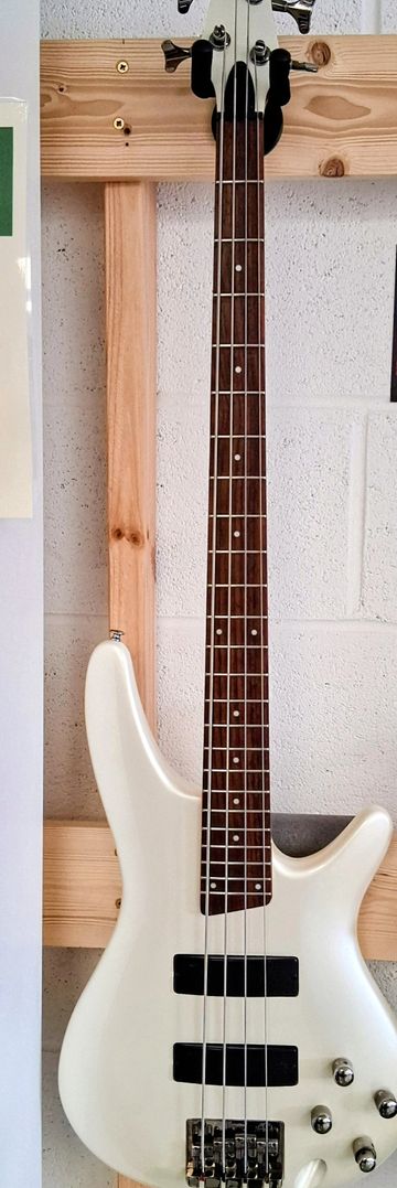 White electric bass guitar hanging on a wooden wall mount.