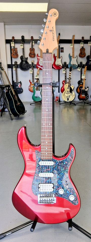 Red Yamaha Pacifica electric guitar with a colorful pickguard on a stand.