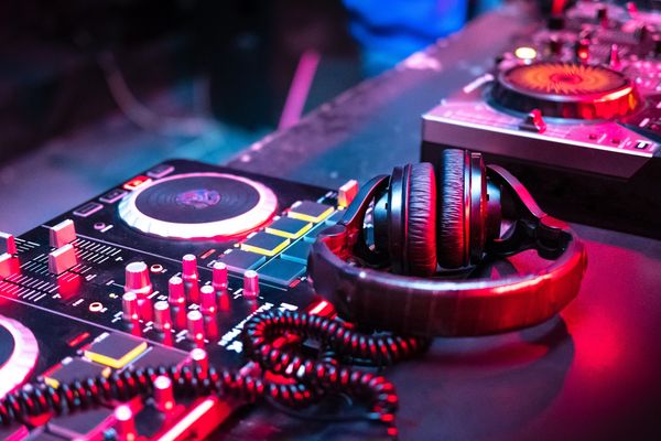 Headphones resting on a DJ mixer with illuminated controls, bathed in red and blue light.
