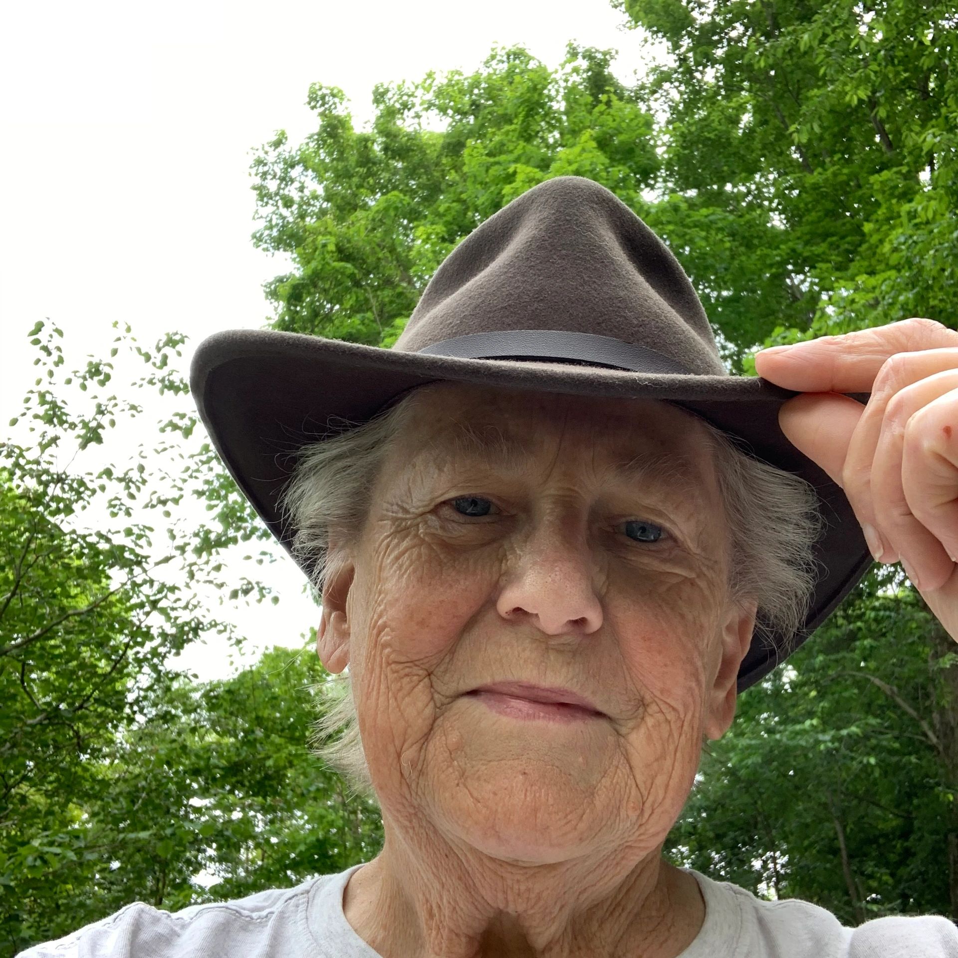 Elderly person outdoors wearing a brown hat and white shirt.