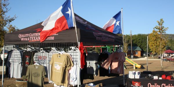 Outdoor stall selling Texan-themed clothing under flags.