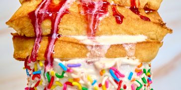 Close-up of a waffle cone with vanilla ice cream and colorful sprinkles topped with syrup.
