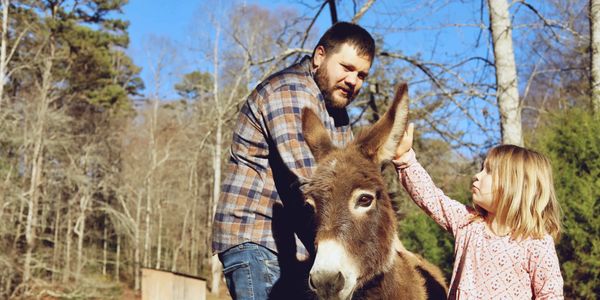 Man and girl petting a donkey outdoors.